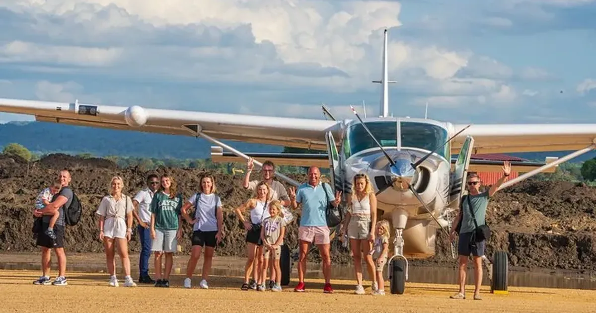 Safari passengers standing in front of a single-engine light aircraft on a dirt airstrip in Tanzania