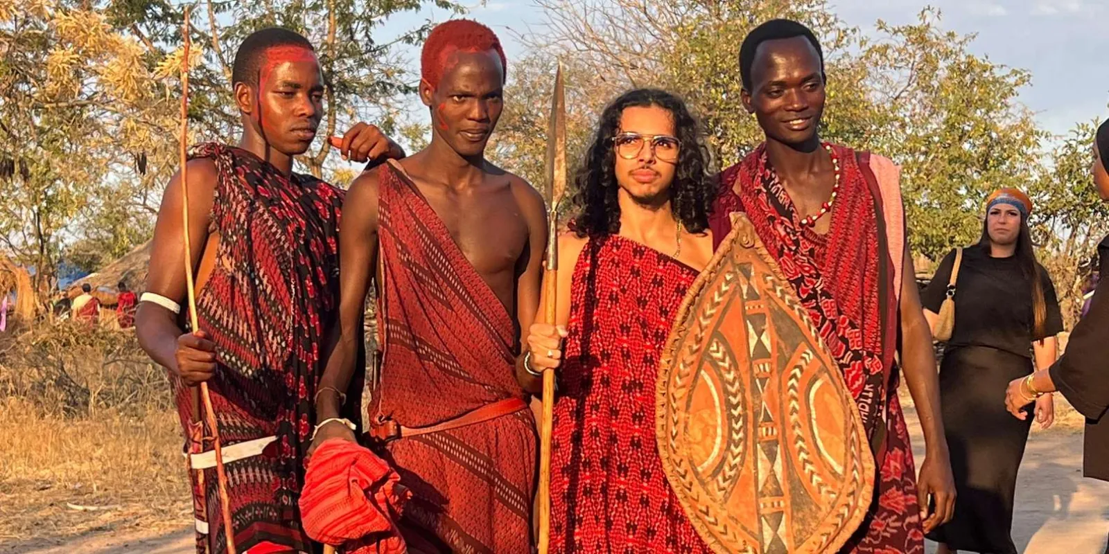 Maasai men with painted faces, spears and a decorated shield welcoming a visitor to their village